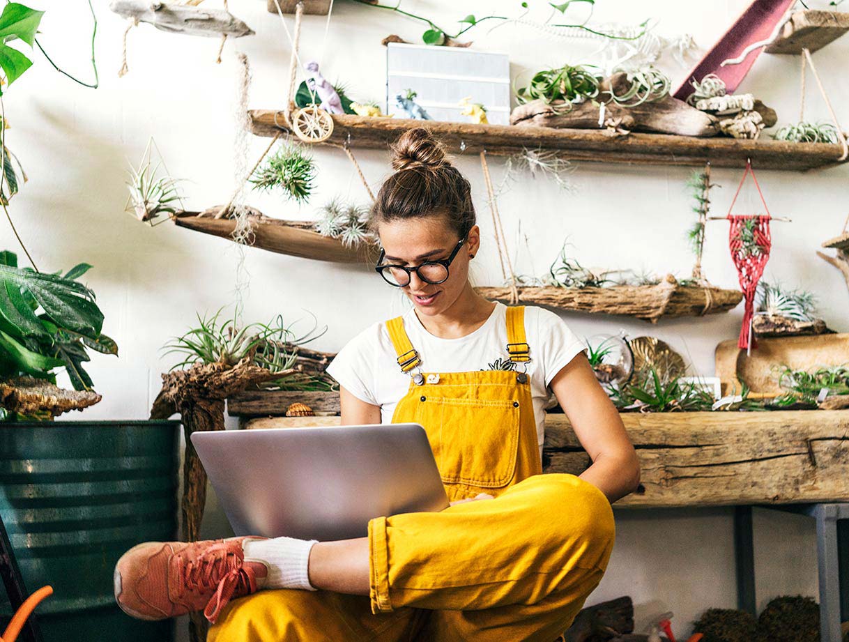 The image shows a woman seated in comfortable surroundings in her home using a computer to make an online payment.